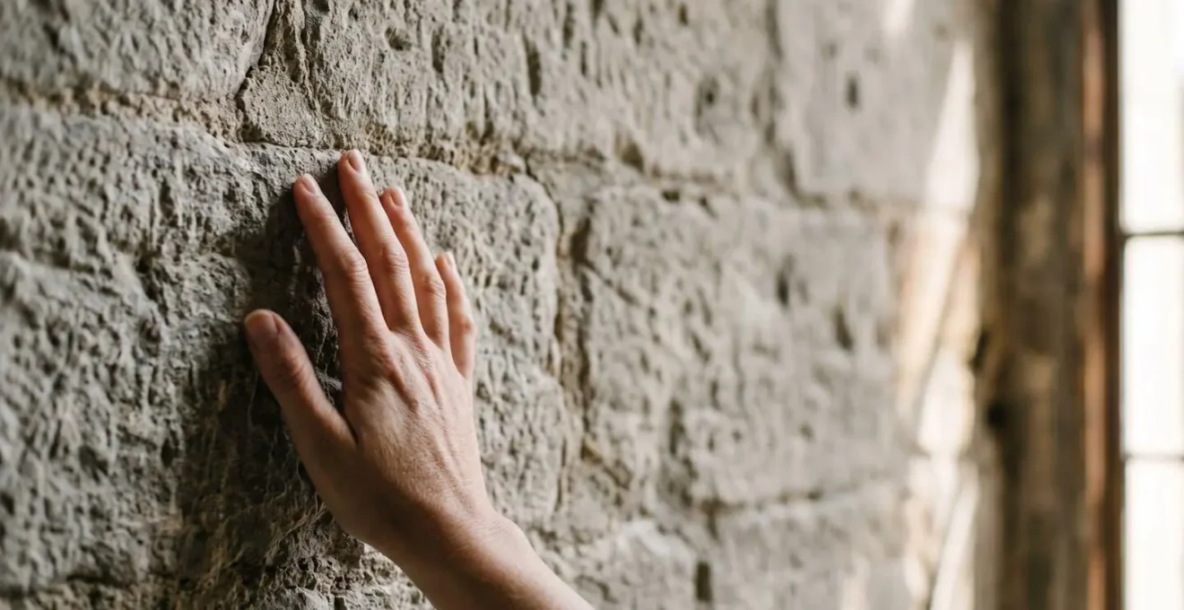 Close-up of a person's hand gently touching weathered medieval stone masonry, showing emotional connection to heritage