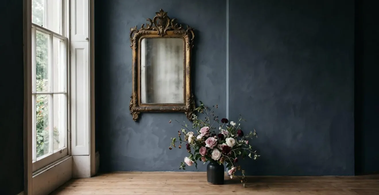 Atmospheric interior corner with single dramatic antique mirror reflecting moody natural light and wild floral arrangement