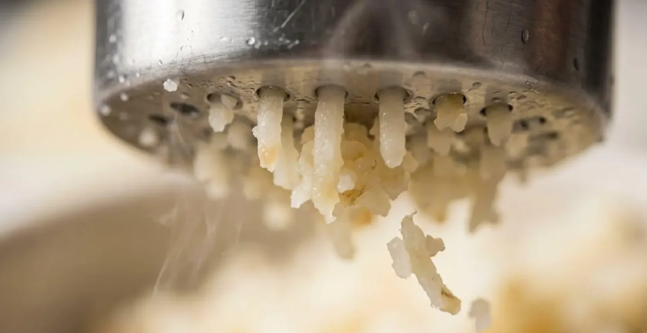Extreme close-up of potato ricer mechanism showing fine extrusion process preserving starch cell structure